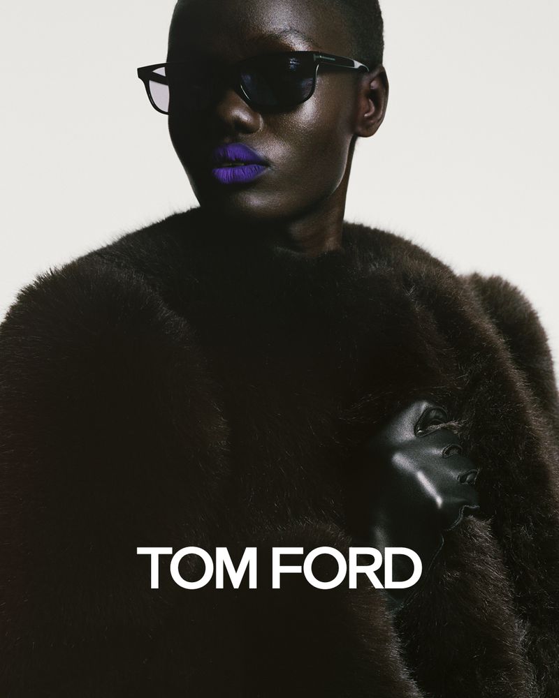 Fashion shot of a dark-skinned woman wearing sunglasses, a fur coat and purple lipstick against a plain background with Tom Ford logo.