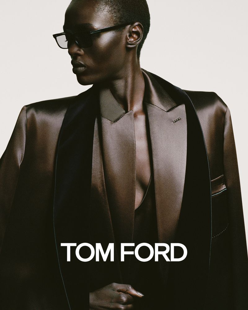 Fashion shot of a Black woman in a satin blazer, sunglasses, and dark lipstick, with the Tom Ford logo visible against a light background.