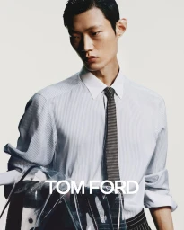 Man wearing a pinstripe button-down shirt and patterned tie holding a transparent bag against a light background.