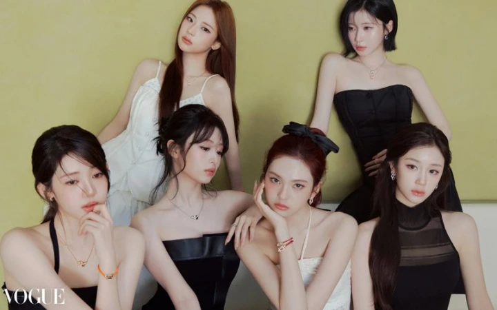 Six young women pose in a group in front of a light yellow wall, wearing black and white strapless dresses and light jewelry for a Vogue shoot.