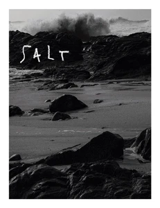 Black and white editorial photograph of a rocky coastline with waves crashing against shore under a white sky.