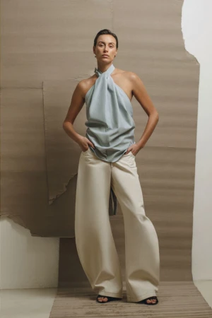 Woman in halter top and wide-leg trousers poses against neutral backdrop in fashion editorial, showcasing minimalist style.