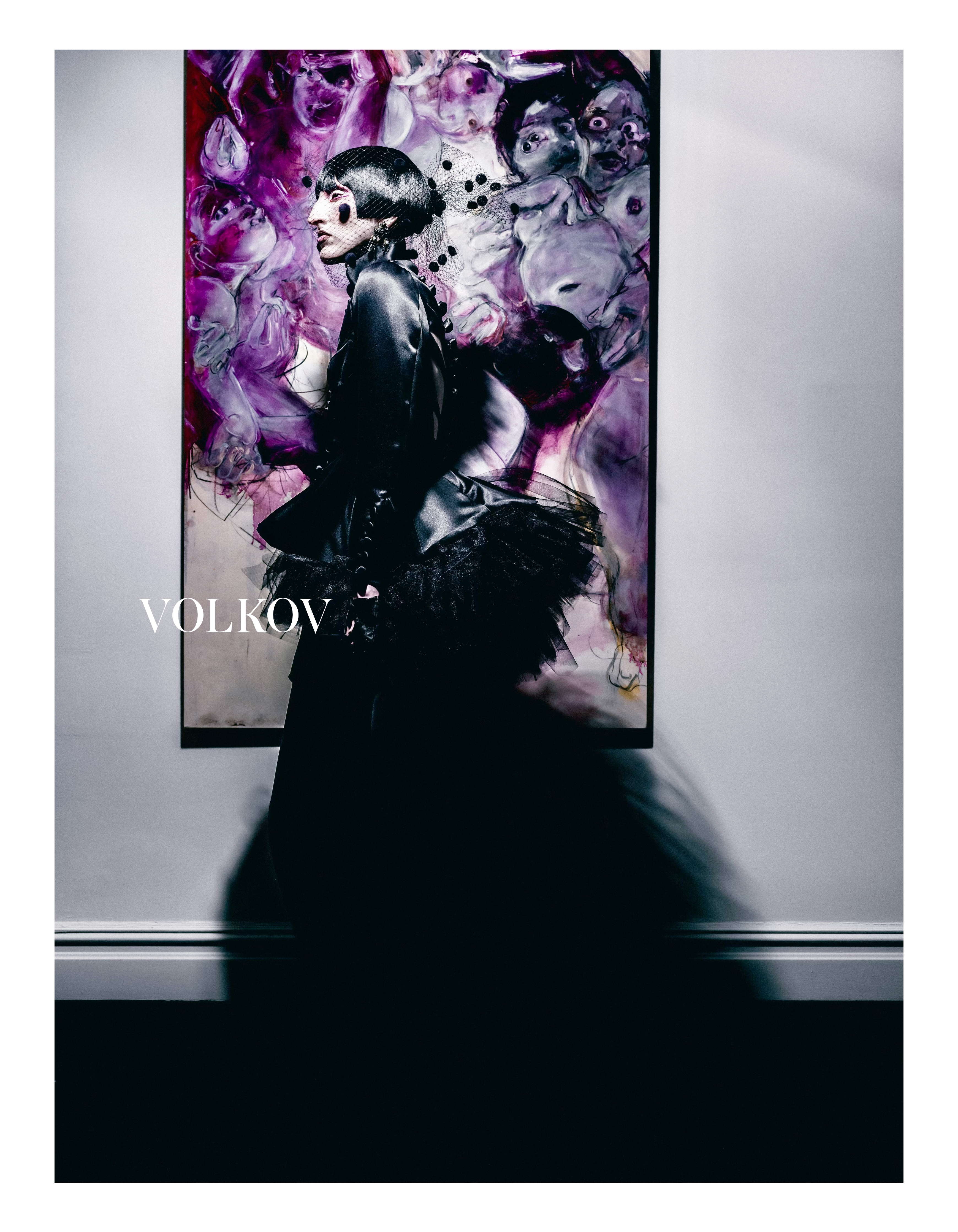 Artistic fashion portrait of a woman in a black dress with bob haircut, posing against an abstract painted backdrop in a photo studio.