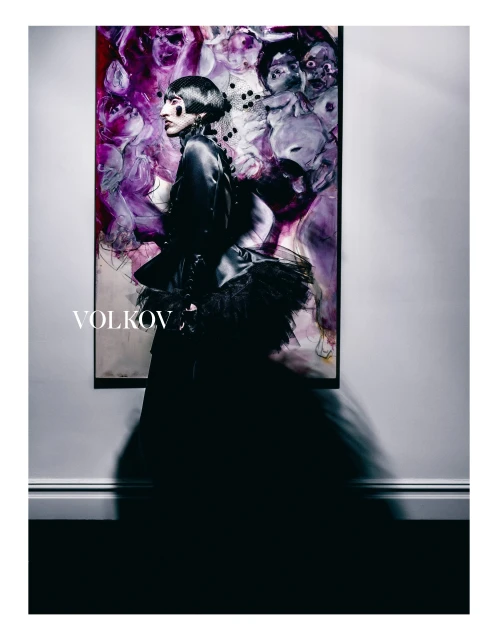 Artistic fashion portrait of a woman in a black dress with bob haircut, posing against an abstract painted backdrop in a photo studio.