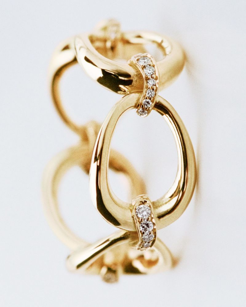Close-up of a golden link bracelet, connected by diamond-studded segments, against a plain white background, in a jewelry advertising style.