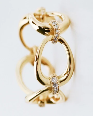 Close-up of a golden link bracelet, connected by diamond-studded segments, against a plain white background, in a jewelry advertising style.