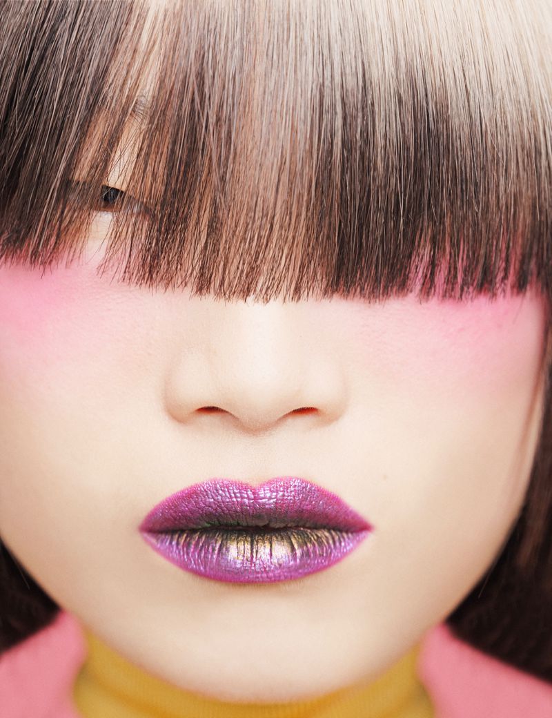 Close-up portrait of an Asian woman with pink eyeshadow and purple lipstick, featuring a distinctive blunt bob haircut with blonde streaks.
