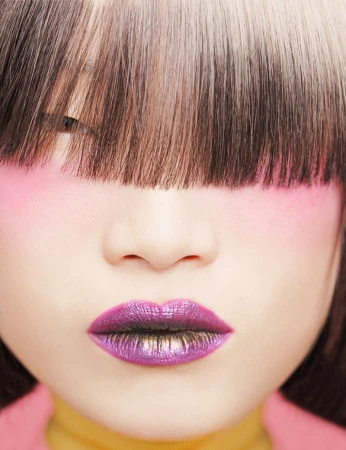 Close-up portrait of an Asian woman with pink eyeshadow and purple lipstick, featuring a distinctive blunt bob haircut with blonde streaks.