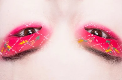 Close-up of a person's eyes featuring vibrant pink eye makeup with white stitched argyle patterns and floral details.