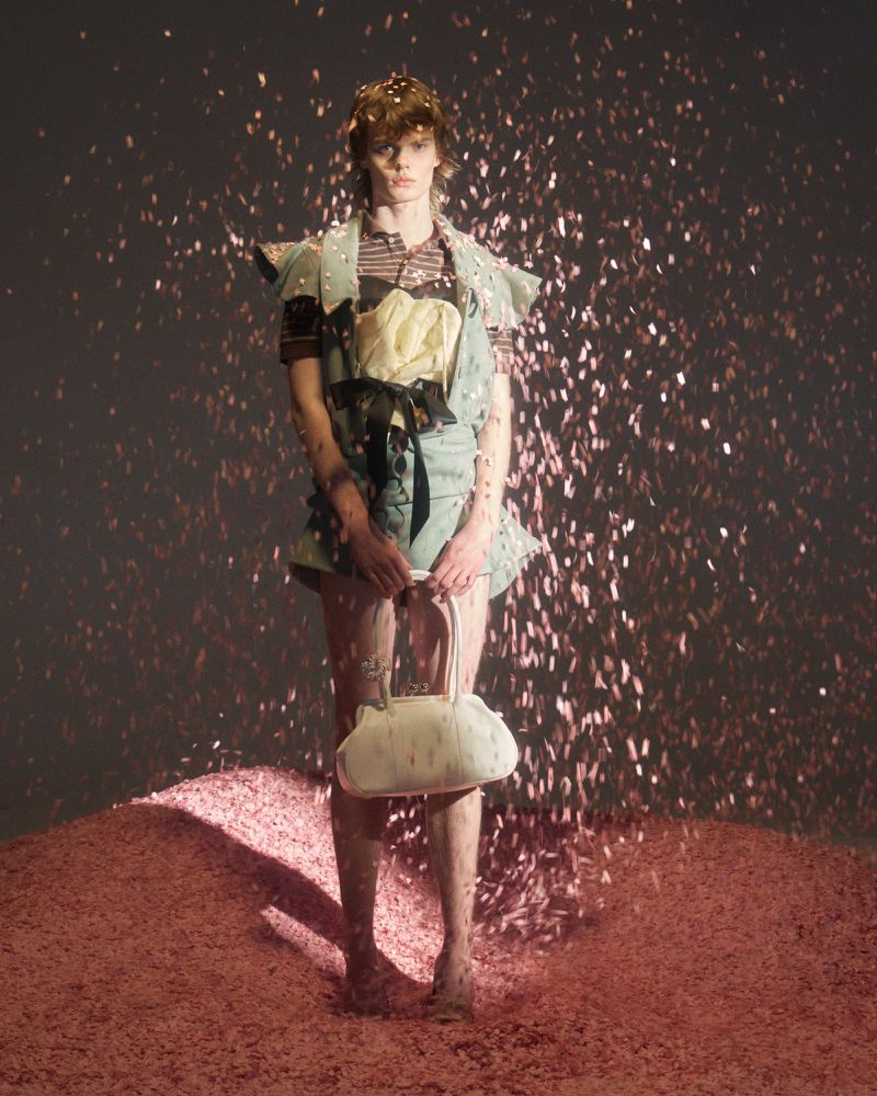 Model standing on a textured pink mound holding a white handbag amidst falling pink confetti for August Barron F/W 2026 editorial