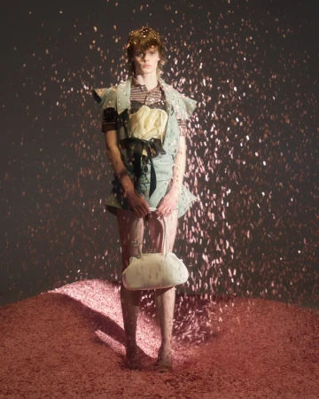 Model standing on a textured pink mound holding a white handbag amidst falling pink confetti for August Barron F/W 2026 editorial