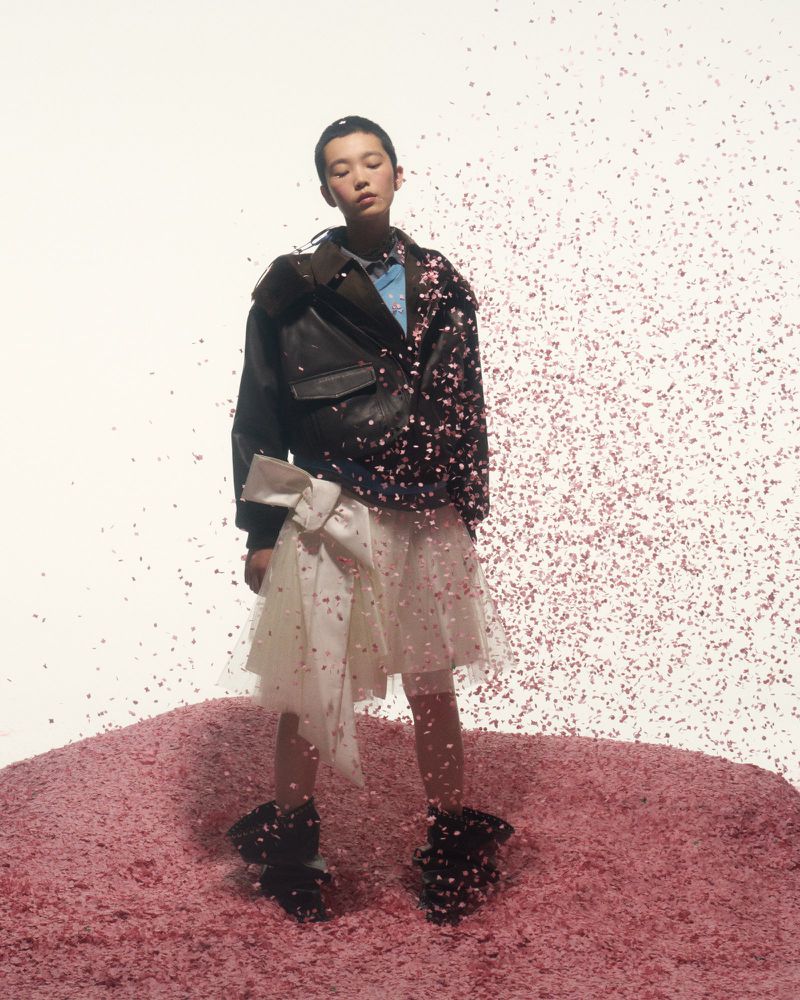 Stylish Asian model posing in an oversized leather jacket and tulle skirt, standing on a mound of pink material with confetti.