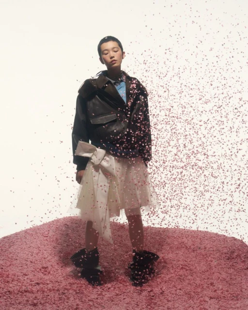 Stylish Asian model posing in an oversized leather jacket and tulle skirt, standing on a mound of pink material with confetti.
