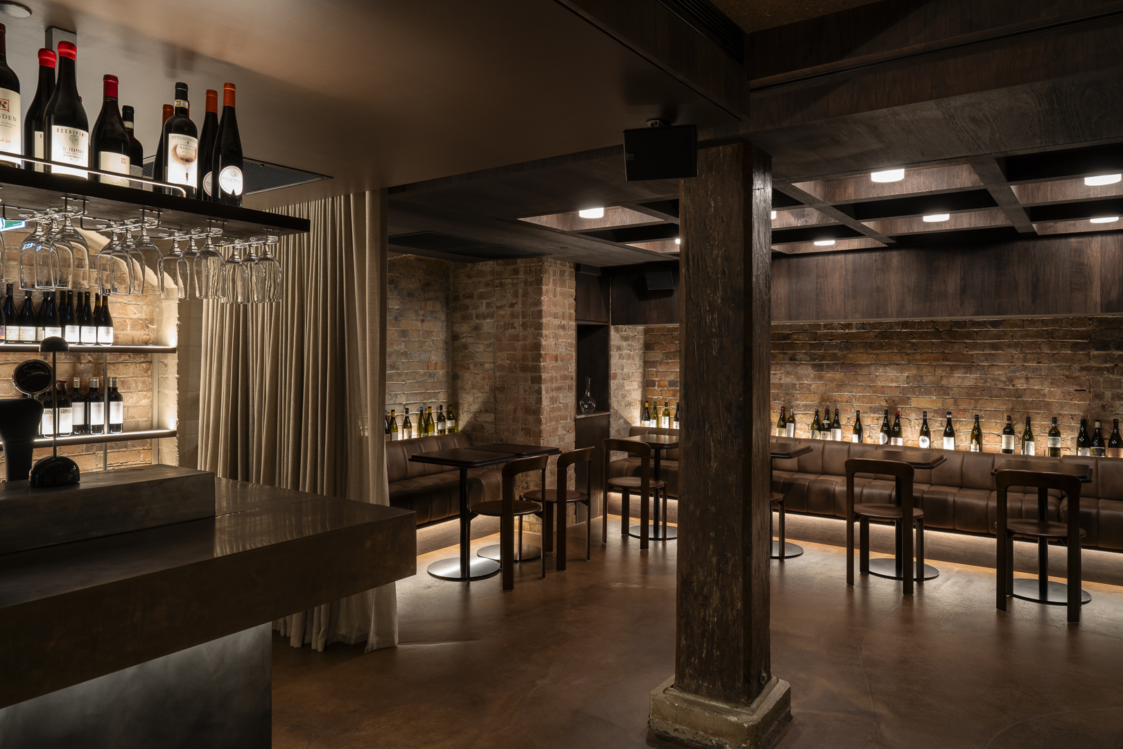 Wine bottles and glasses displayed on shelves in a dimly lit wine bar with tables and chairs, creating an intimate atmosphere.