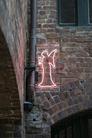Neon sign of an angel holding a glass on a brick wall. The sign is illuminated with red neon and has a modern, minimalist design.