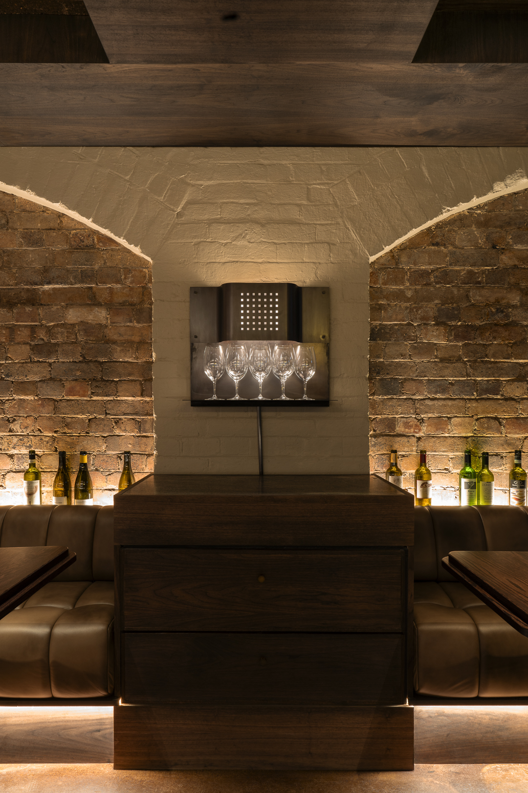 Upscale restaurant interior showcasing a wood bar, leather booths, and wine bottle display, illuminated with warm lighting and brick details.