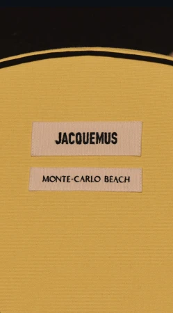 Close-up of a yellow fabric item featuring two labels with black text reading 'JACQUEMUS' and 'MONTE-CARLO BEACH' respectively.