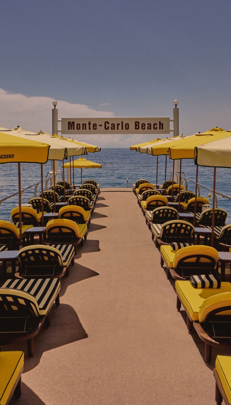 Seascape view of rows of black and yellow striped sunbeds with yellow umbrellas along a sandy path towards the ocean.