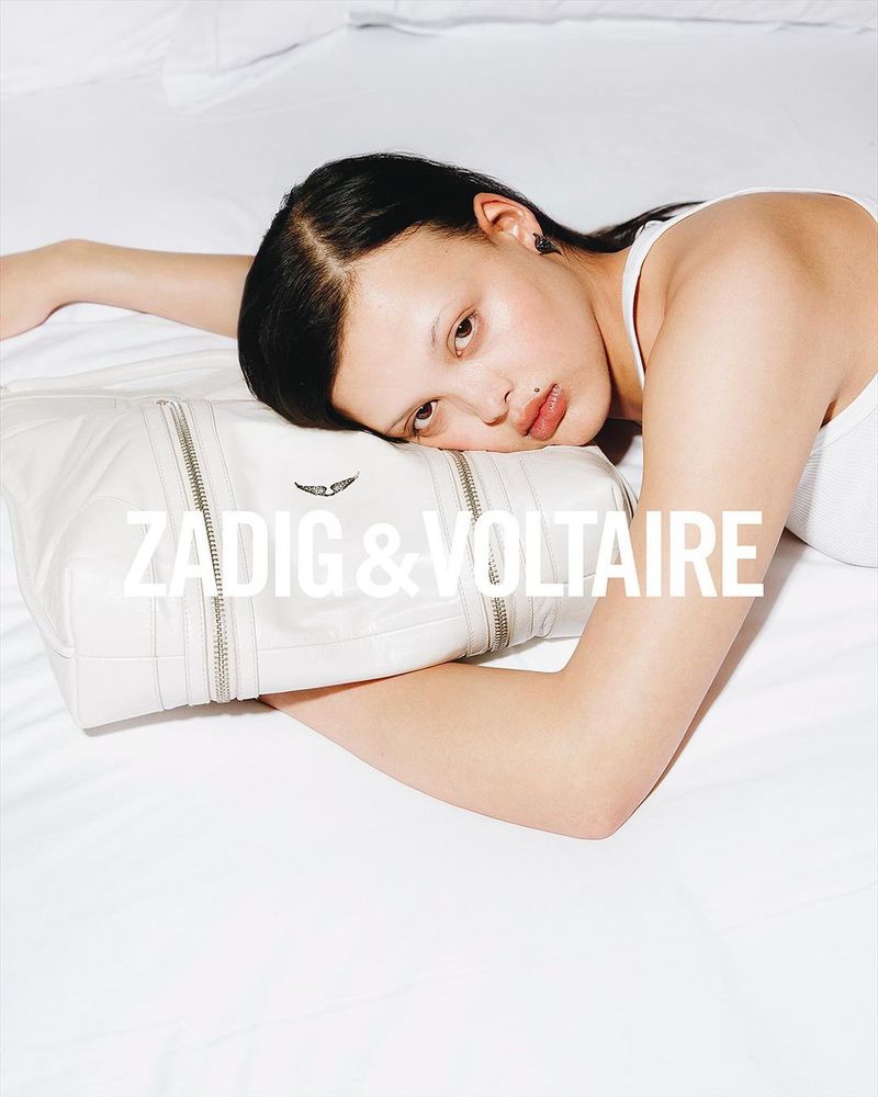 A young woman rests on a white pillow with a white handbag from Zadig & Voltaire, shot with studio lighting and a shallow depth of field.