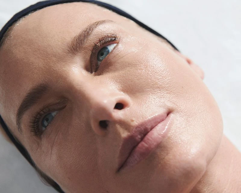 Close-up portrait of a fair-skinned woman with blue eyes wearing a black headband. Soft lighting highlights the model's clean skin.