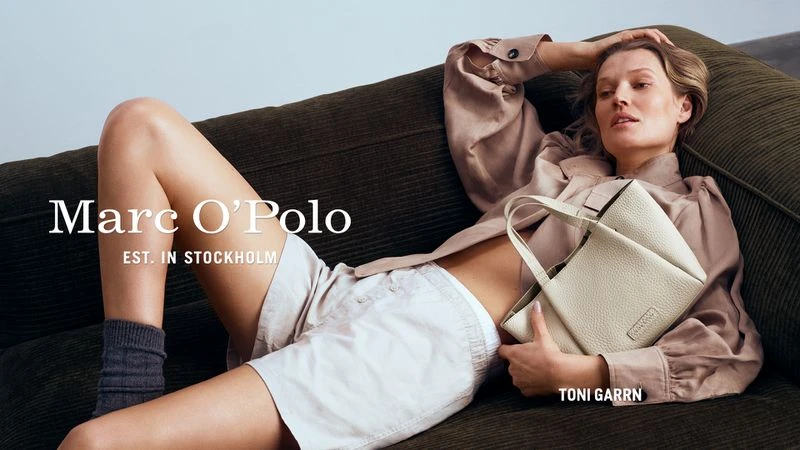 Toni Garrn lies on a corduroy couch, modeling Marc O'Polo purse in a fashion editorial shot with natural lighting and casual styling.