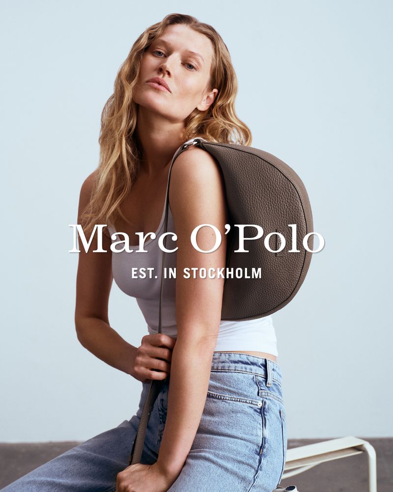 A woman poses with a satchel bag in a studio setting, wearing a white top and light wash jeans, advertising for Marc O'Polo.
