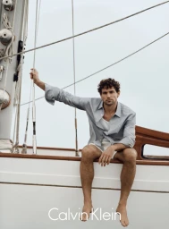 Model Giacomo Cavalli sitting on a sailboat deck wearing a light blue shirt under an overcast sky.