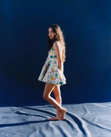 Young woman in floral dress poses in photo studio. Portrait shot with blue backdrop, her dark hair cascading down her shoulders.