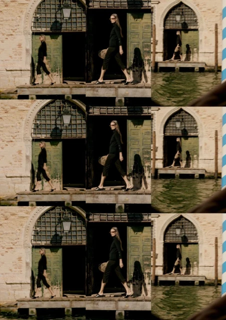 Woman in black outfit walks past weathered building with open doors next to water in Venice, Italy in outdoor, eye-level, medium shot.