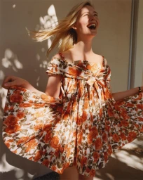 Elle Fanning laughing outdoors wearing an orange floral dress with hair blowing in the wind in a Vogue Espana portrait.