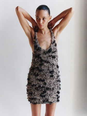 Model Binx Walton wearing a textured knit dress with arms raised against a seamless white background for Holiday Magazine