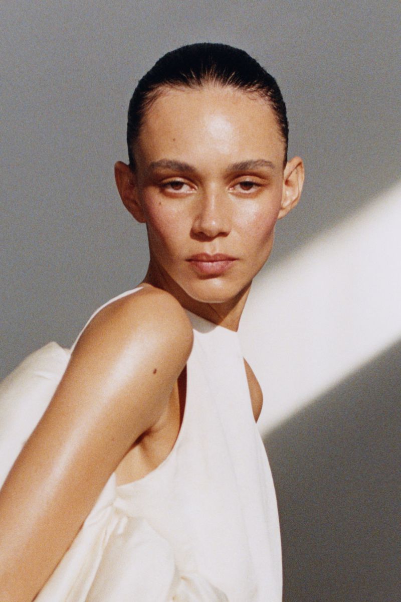 Portrait of a woman with sleek hair and a white dress against a bright background with shadows, shot in a photo studio.