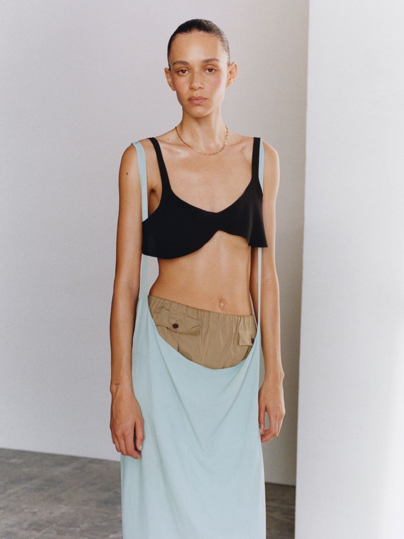 Fashion shot of woman in black top and long light blue skirt, posing in studio with fair skin and neutral expression in vertical format.