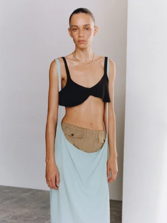 Fashion shot of woman in black top and long light blue skirt, posing in studio with fair skin and neutral expression in vertical format.