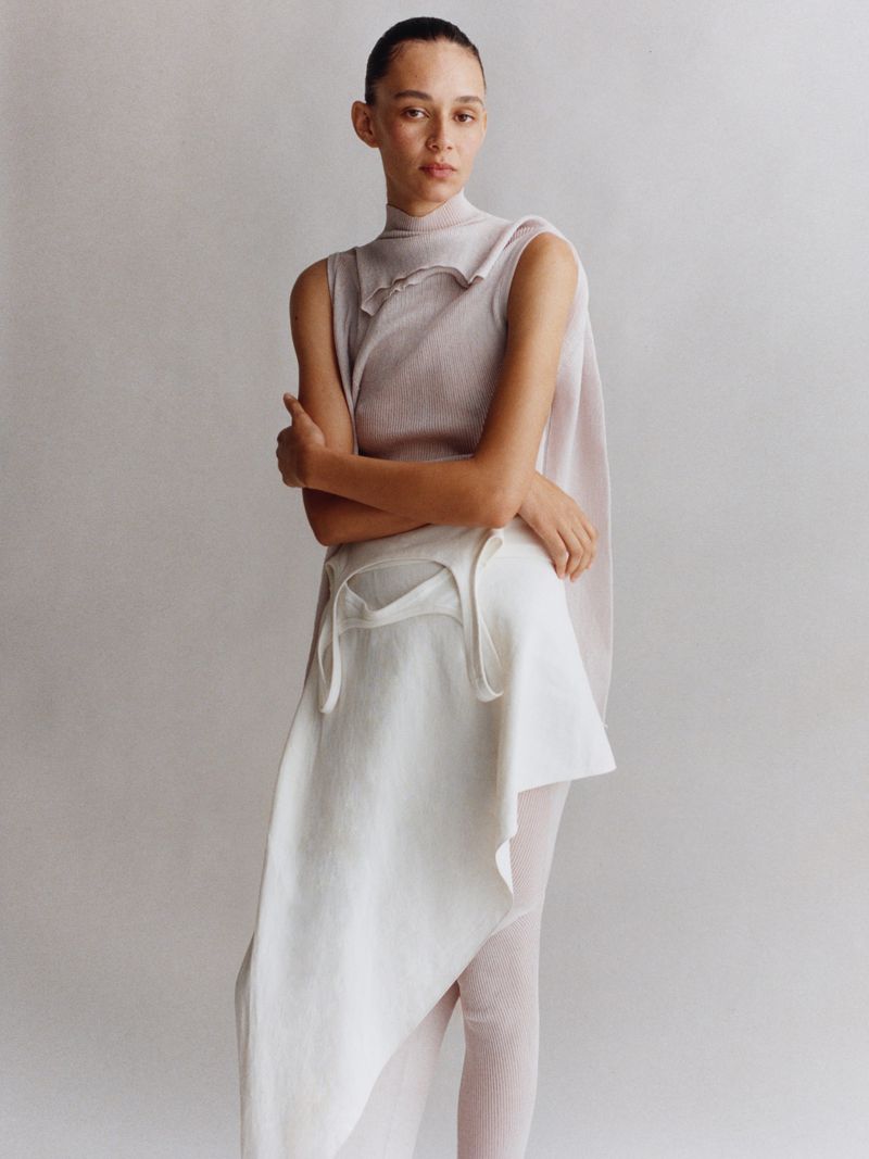 Fashion shot of a woman in a sleeveless top and layered skirt, posing in front of a neutral background, focusing on textures and fabrics.
