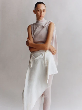 Fashion shot of a woman in a sleeveless top and layered skirt, posing in front of a neutral background, focusing on textures and fabrics.