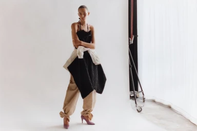 Model Binx Walton in a black top and beige trousers posing in a studio for Holiday Magazine captured by Krisztián Éder