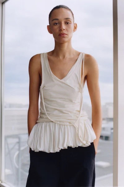 Model Binx Walton wearing a cream top and dark trousers in an editorial portrait for Holiday Magazine.