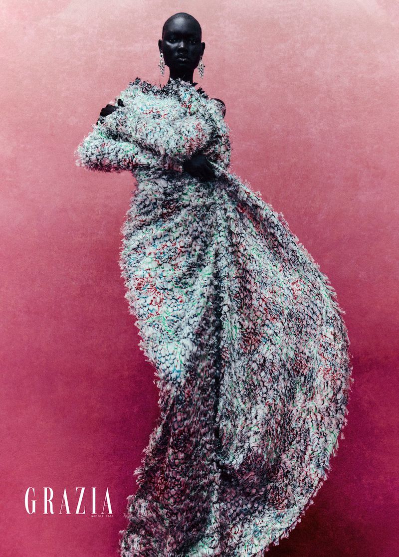 Fashion editorial shot of a Black female model in a textured gown with earrings, posing against a pink textured backdrop.  