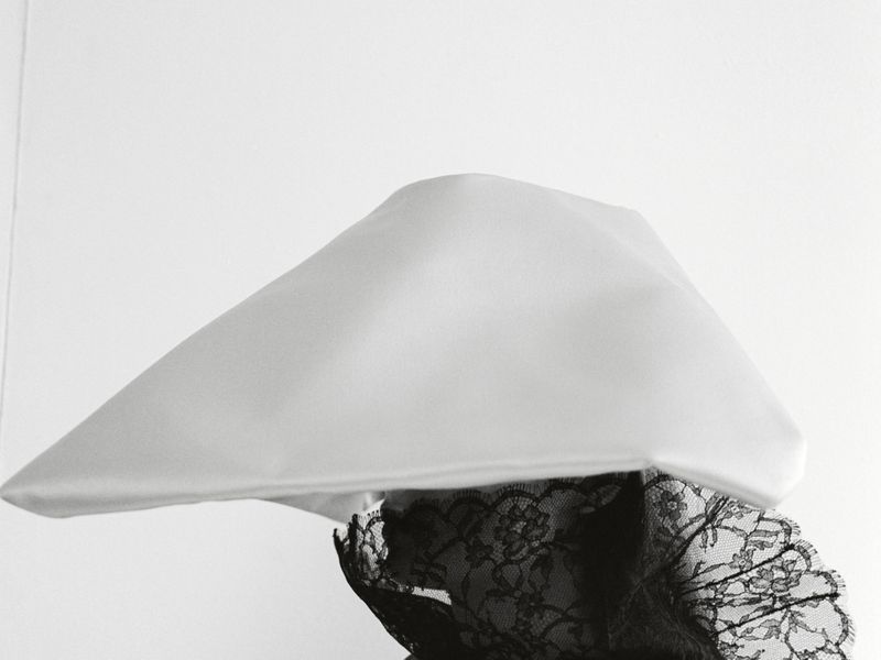 Close-up studio shot of a white geometric hat adorned with black lace, creating a sophisticated and high-contrast fashion statement.