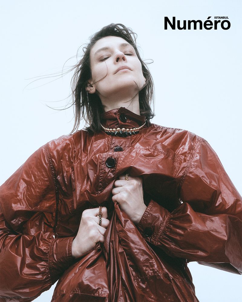 Woman in a red coat poses outdoors against a light sky, adorned with a gold necklace and rings. The Numero Istanbul magazine logo is visible.