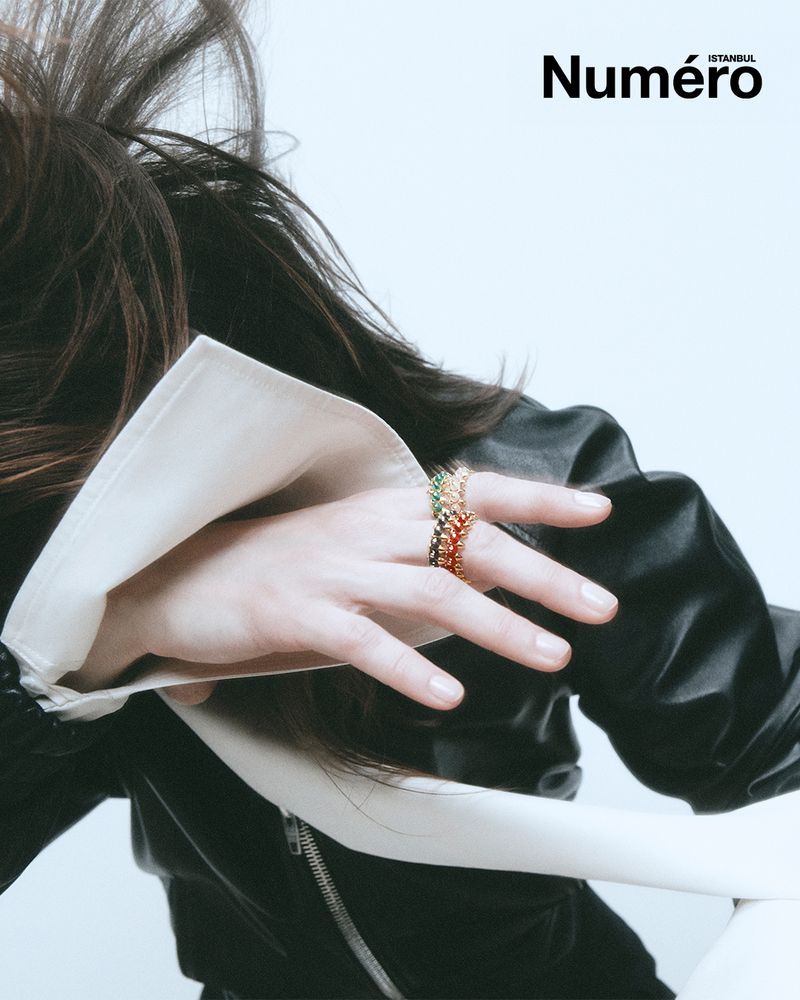 Close-up shot showcasing an adult female hand adorned with stackable rings, complemented by a black jacket and an off-white collar.