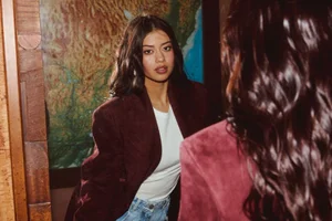 Amber Midthunder looking in a mirror wearing a burgundy blazer over a white t-shirt and blue jeans, photographed by Sami Drasin for Grumpy Magazine.