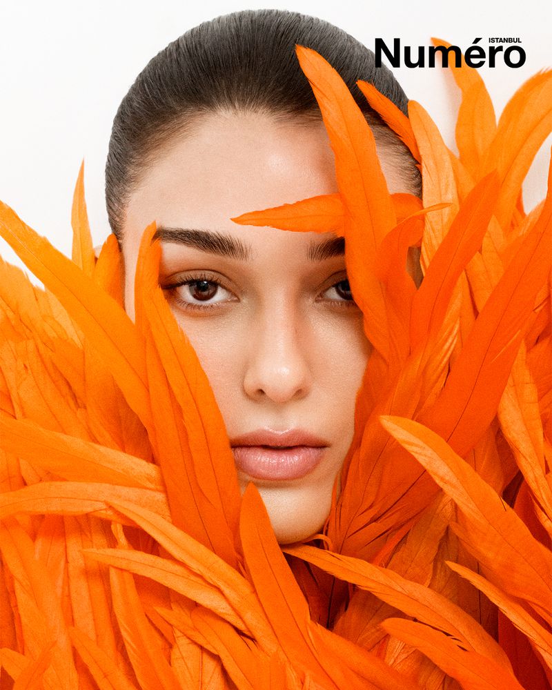 Close-up portrait of a woman surrounded by bright orange feathers against a white background, with visible 'Numero' magazine text.