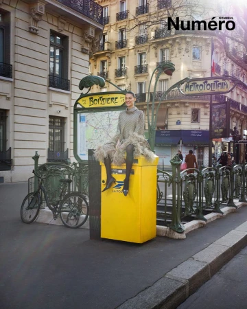 An adult woman in an ornate dress sits on a yellow La Poste mailbox near the Boissière Métro station in Paris on a sunny day.