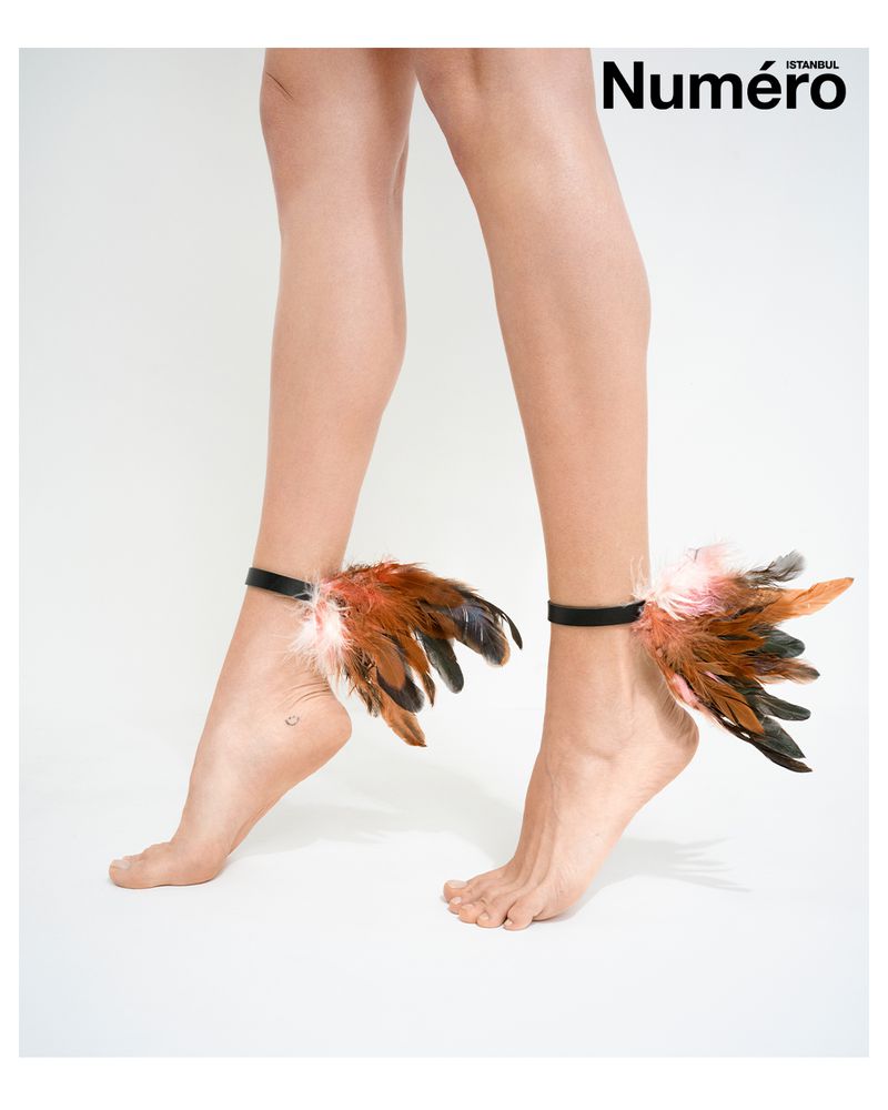 Woman's feet adorned with feathered anklets on a white background, fashion editorial style, with 'Numero' magazine logo visible.