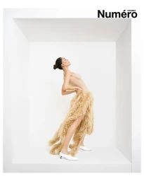 Model in a textured fringed garment and white heels posing inside a minimalist white alcove set for Numéro Istanbul