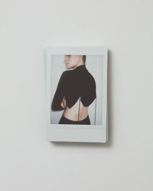 Polaroid image featuring a woman in a black top with an open back, arms crossed, and looking to the side against a white background.