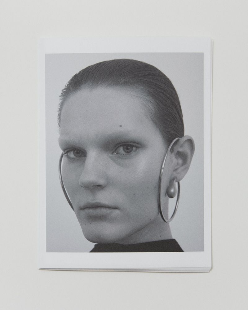 Monochrome portrait of a woman with large, circular earrings, set against a neutral background, showcasing a minimalistic aesthetic.