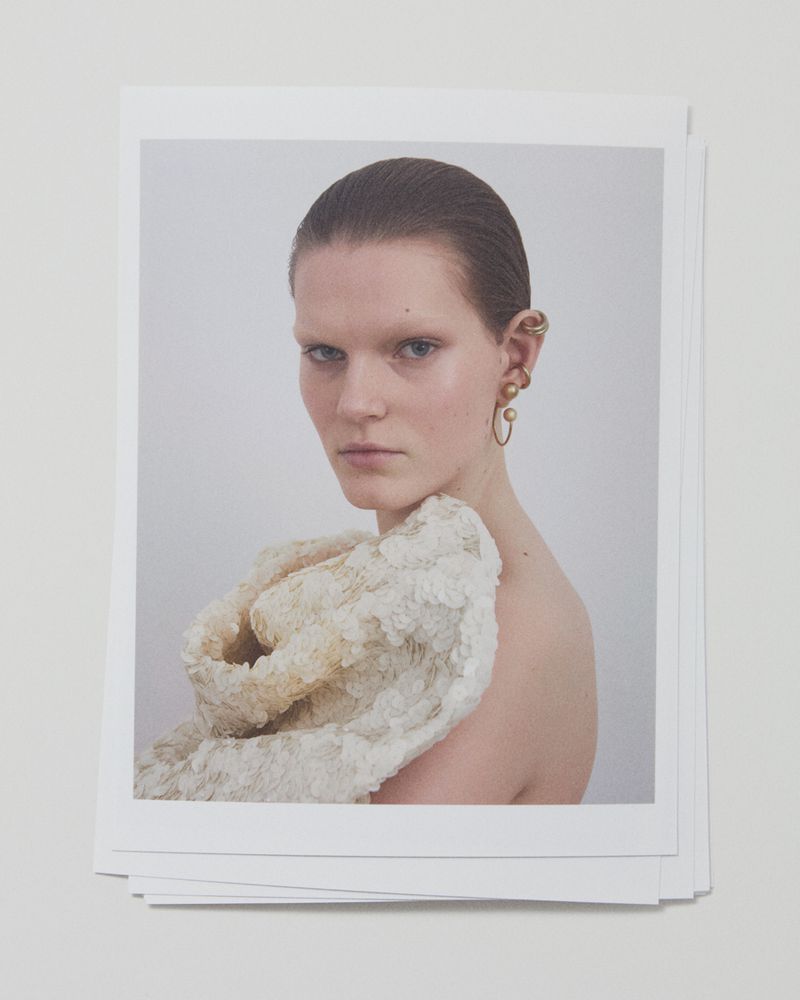 Portrait of a woman with golden earrings and a textured shawl posing in a photo studio against a soft white background.